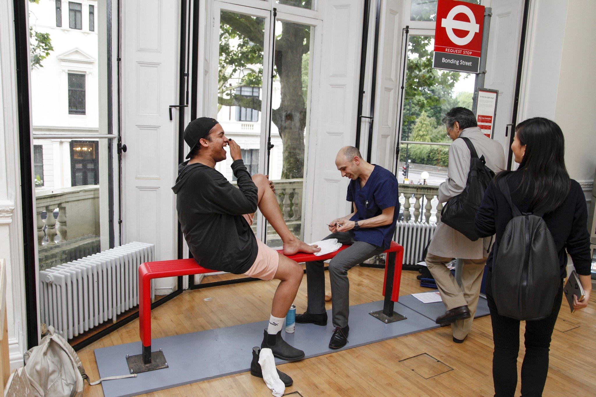 Michael treating a patient at a pop-up foot clinic, styled as a London bus stop, at a design exhibition